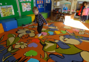 Chłopiec przechodzi po ułożonej na dywanie ścieżce z serc, w tle ustawione dzieci w rzędzie.